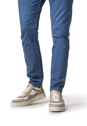 Sneaker mit einem Obermaterial aus cremefarbenem und grauem Wildleder, beigen Akzenten, weißen Schnürsenkeln und einer strukturierten Gummisohle. Getragen mit blauen, eng anliegenden Hosen.