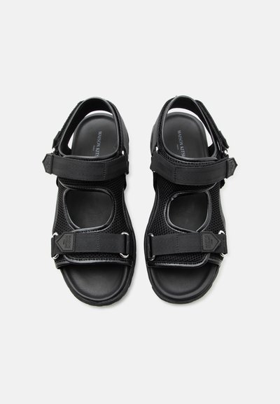 Μαύρα σανδάλια με ανοιχτά δάχτυλα, ρυθμιζόμενους ιμάντες, επάνω μέρος από δίχτυ, αναπαυτική εσωτερική σόλα και εμφανές το όνομα της μάρκας "Maison Kitsuné" στο εσωτερικό.