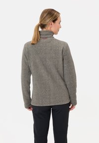 Grijze fleece pullover met hoge kraag, met een ontwerp van platte naden, zachte textuur en een kleine rode accent op de achterkant van de halslijn.