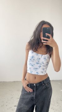 Fehér virágmintás crop top gyűrt részletekkel, magas derekú fekete farmernadrággal párosítva. Sima anyag, világoskék virágminta.