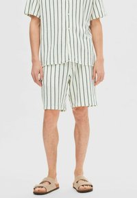 Trumpetėlės su trumpomis rankovėmis ir atitinkančios šortai iš lengvos, tekstūruotos medžiagos. Balti su žaliais vertikaliais dryžiais. Atsitiktinės šlepetės užbaigia įvaizdį.