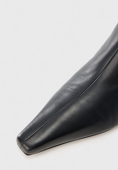 Μαύρο δερμάτινο παπούτσι με μυτερή μύτη, που διαθέτει λεία υφή και διακριτικές ραφές, στενεύοντας σε μια αιχμηρή άκρη.