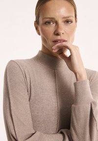 Jasnobrązowy sweter z wysokim dekoltem, wykonany z miękkiej dzianiny, z długimi rękawami i ściągaczami oraz prostym, eleganckim krojem.