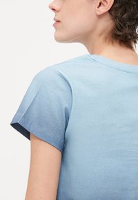Hele sinine lühikeste varrukatega t-särk, millel on sile tekstuur, klassikaline ümar kaelus ja õrn gradient tumedamatest heledamatesse tooni.