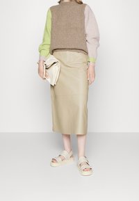 Pull en maille marron, vert et rose, associé à une jupe midi en cuir marron clair et des sandales à plateforme beige avec des accents cloutés.