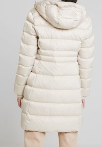 Beige puffer coat with horizontal quilted design, padded fabric, and adjustable hood. Features ribbed cuffs and longer length for coverage.