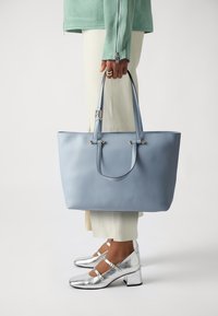 Borsa a spalla azzurro chiaro con manici doppi, texture in pelle liscia, dettagli in tonalità oro, forma rettangolare e senza chiusura visibile.