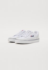 White canvas sneakers with textured quilted detail, sturdy rubber sole, and navy striped accent along the bottom. Fila logo on the side.