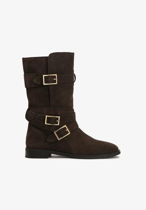 Brązowe zamszowe kozaki za kolano z trzema dekoracyjnymi paskami z złotymi klamrami. Okrągły czubek i solidna czarna podeszwa. Gładka tekstura.