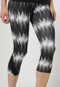 Czarno-białe legginsy capri z paskowanym, szczotkowanym wzorem, wykonane z elastycznego materiału, charakteryzujące się gładką teksturą i dopasowanym krojem.