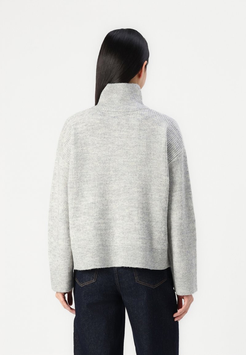 Szary żebrowany sweter z golfem, z długimi rękawami i krótkim krojem, w połączeniu z ciemnoniebieskimi dżinsami. Miękka tekstura i luźny krój.