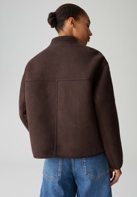 Giacca marrone oversize con una texture morbida e colletto a coste; presenta un retro semplice ed è abbinata a jeans azzurri dalla vestibilità ampia.