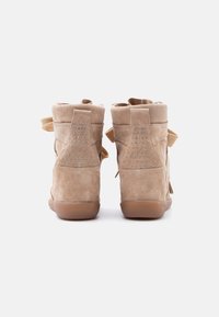 Μπεζ σουέντ πλατφόρμες αθλητικά παπούτσια, εμφανιζόμενα από πίσω, με μεταλλικές τρύπες για κορδόνια στα πλαϊνά πίσω μέρη και μπεζ κορδόνια, σε λευκό φόντο.