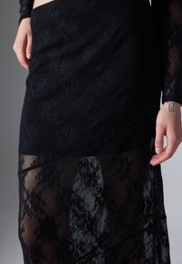 Svarte blonde skjørt med lagdelt design og gjennomsiktig stoffoverlegg, intrikate blomster mønster og elastisk midjebånd. Teksturen er myk og delikat.