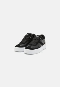 Black sneakers with a smooth leather and textured suede upper, white platform sole, and laces, featuring a logo on the tongue.
