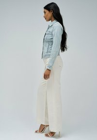 Veste en denim bleu clair au design ajusté avec deux poches avant, associée à un pantalon large crème et des sandales à talons hauts.