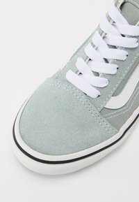Sneaker in suede grigio chiaro con lacci bianchi, suola in gomma e dettagli laterali. Punta arrotondata e accenti di cucitura discreti.