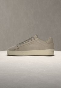 Baskets basses gris clair avec lacets et semelle blanche épaisse sur une surface claire et un fond neutre.
