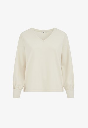 Dolga majica z V-izrezom v svetlo kremni barvi, z otipno tekstilijo, rahlo napihnjenimi rokavi in prilegajočimi manšetami za sproščen oprijem.