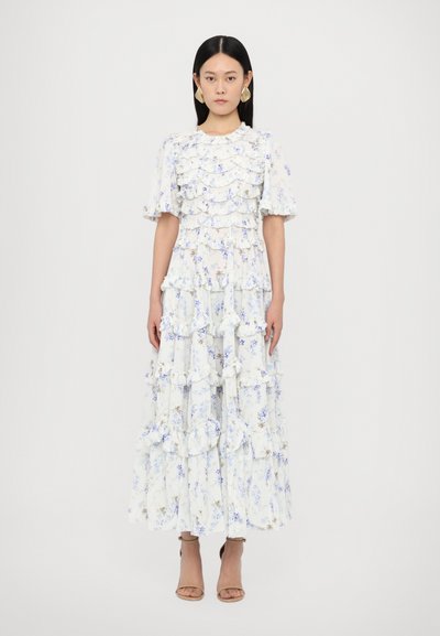 Maxikleid mit floralem Druck in Weiß mit Lavendel- und blauen Blumen. Verfügt über Rüschentierchen und kurze Puffärmel. Kombiniert mit sandfarbenen Riemchensandalen.