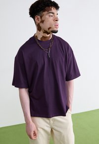 Lilla kortærmet t-shirt med løs pasform. Blødt stof, rund hals og brede ærmer. Bæres med beige bukser og lagdelte halskæder.