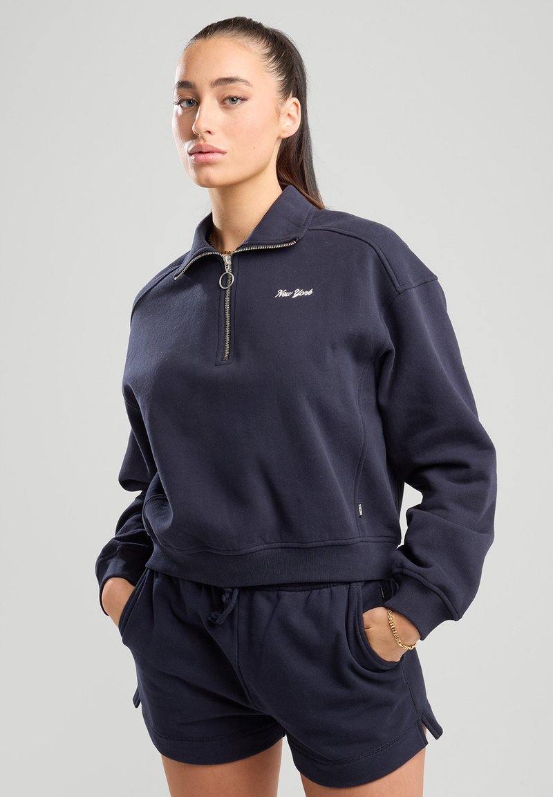 Tummansininen vetoketjuhuppari ribbineuloksilla varustetuilla hihoilla ja helmalla, jossa on "New York" -kirjonta rinnassa. Yhdistetty samanlaisisiin shortseihin.