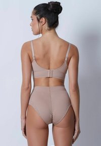 Beige underkläder set bestående av en sömlös bralette med justerbara axelband och en högmidjad trosor med vågig fåll och texturerad tyg.