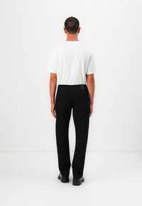 Pantalons en denim noirs à coupe droite, dotés de poches arrière et d'une étiquette discrète au niveau de la taille. Portés avec un t-shirt blanc uni.