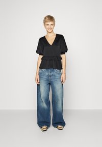 Top peplum in satin nero con scollo a V e maniche corte a sbuffo, abbinato a jeans a gamba larga blu sbiaditi e scarpe metallizzate. Design semplice, senza motivi.