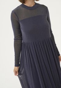 Mörkblå långärmad klänning med en figurnära överdel och utsvängd kjol. Genomskinligt övre parti med subtil glittern effekt. Mjuk, flödande tygtextur.