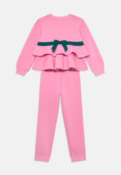 Rosa Sweatshirt- und Hosen-Set. Das Oberteil hat ein mehrlagiges Design mit einer türkisfarbenen Schleifenapplikation an der Taille. Weicher Stoff, gerippte Bündchen und Saum.