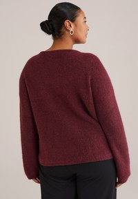 Burgundy tröja med en mjuk, fluffig textur, med rund halsringning och sänkta axlar, kombinerad med svarta byxor.
