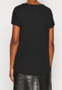 Černé tričko s krátkým rukávem vyrobené z měkké bavlny. Má kulatý výstřih a mírně zakřivený lem. Bez výrazných vzorů nebo detailů.
