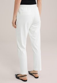 Bílé kalhoty s úzkým střihem, mají elastický pás a dvě zadní kapsy. V kombinaci s černými plochými sandály.