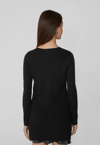 Schwarzes, geripptes Strickkleid mit langen Ärmeln und Rundhalsausschnitt, das eine etwas kürzere Länge aufweist. Glatte Textur und minimale Details.