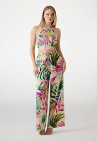 Completo a due pezzi composto da un top cropped e pantaloni a gamba larga. Realizzato in un tessuto leggero con un motivo di foglie tropicali colorate in verde e rosa.
