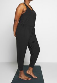 Combinaison noire sans manches avec un haut ajusté, une taille élastique et des jambes fuselées. Tissu doux avec une texture lisse et un design minimal.