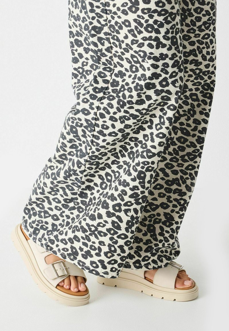 Leopard print wide-leg pants in beige and black, paired with cream platform sandals featuring two adjustable straps and a chunky sole.