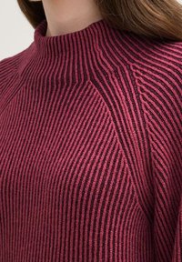 Sweter z wysokim kołnierzem w głębokim burgundowym kolorze, z pionowym prążkowanym wzorem i kontrastującymi ciemnymi paskami na ramionach.