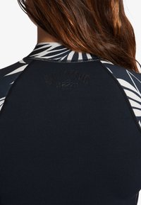 Parte superior de traje de neopreno en color azul marino con un patrón geométrico en blanco y negro que contrasta en el cuello y los hombros. Detalle del logo texturizado.