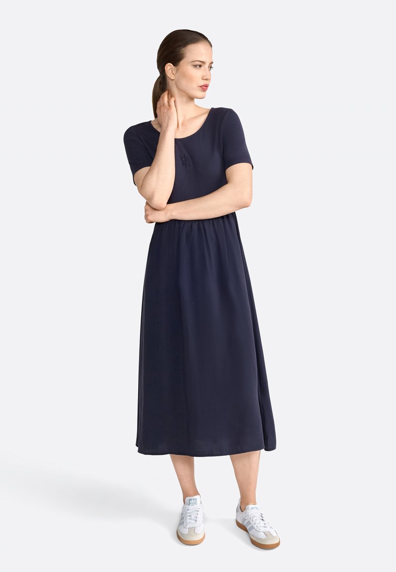 Robe midi bleu marine avec un haut ajusté, des manches courtes et une taille froncée, associée à des baskets blanches et peu de détails.