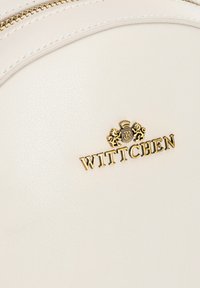 Zaino strutturato bianco realizzato in materiale sintetico testurizzato. Presenta un accento dorato con il logo "WITTCHEN" e un emblema decorativo.