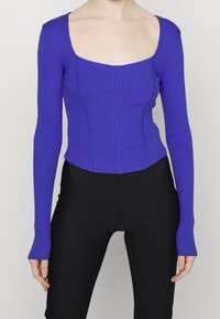 Fioletowa, prążkowana bluzka z długim rękawem, z kwadratowym dekoltem i dopasowanym krojem, z detalami szwów i skróconym dołem. W komplecie z czarnymi spodniami.