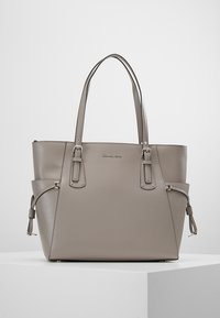 Sac tote en cuir gris grainé avec deux poignées supérieures, des sangles latérales réglables et un logo subtil à l'avant. Forme lisse et structurée.