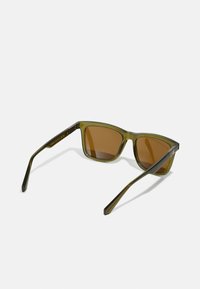 Ochelari de soare de culoare verde, cu lentile dreptunghiulare, lentile maro și brațe elegante. Prezintă branding pe lateral și un finisaj mat.