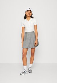 Biele polo tričko, sukňa s čierno-bielym houndstooth vzorom, biela šiltovka a vzorované tenisky. Krátke rukávy, priliehavý strih, neformálny štýl.