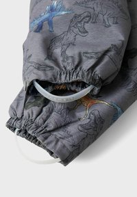 Grått tyg med dinosaurillustrationer, försedd med elastiska muddar och synliga dragskor. Materialet har en slät textur med färgglada detaljer.