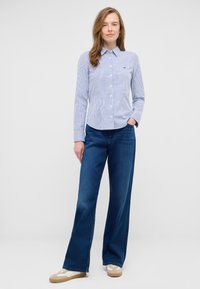 Blue and white striped button-up shirt with a collar, paired with wide-leg dark denim jeans and light-colored sneakers.