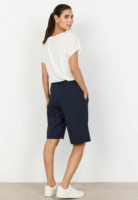Navy bermuda shorts with side pockets, tailored fit, and a smooth texture. Paired with a white short-sleeve t-shirt and white sneakers.