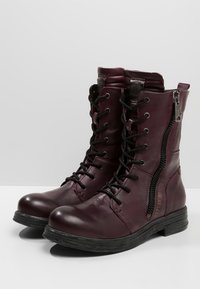 Stivali lace-up color bordeaux scuro con cerniere laterali, caratterizzati da una punta arrotondata e una suola nera testurizzata su uno sfondo grigio chiaro.
